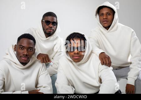 Groupe de gars afro-américains en sweats à capuche marron posant sur un fond blanc. Deux en lunettes de soleil. Banque D'Images