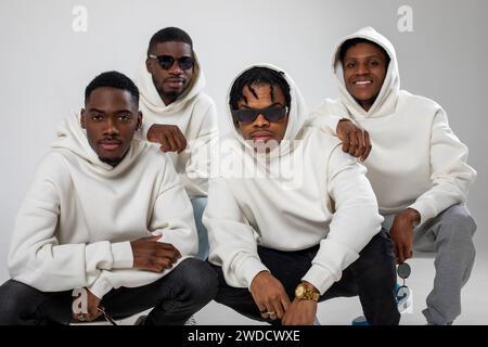 Groupe de gars afro-américains en sweats à capuche marron posant sur un fond blanc. Deux en lunettes de soleil. Banque D'Images