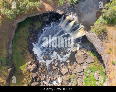 Vue aérienne d'une chute d'eau tombant sur un rebord rocheux dans un grand cratère ouvert aux chutes de Wannon dans l'ouest du Victoria, Australie. Banque D'Images