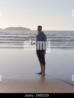 Beau jeune homme souriant avec le signe pouces vers le haut debout sur une plage à Essaouira, Maroc, 19 janvier 2024 Banque D'Images