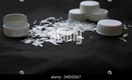 Macro shot sur un tas de microparticules de plastique désintégrées à côté de bouchons de bouteilles en plastique et de sacs poubelles. Vieux microplastique décomposé et décomposé Banque D'Images