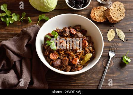 Ragoût de chou (bigos polish) avec choucroute, champignons, viandes fumées et épices dans un bol blanc sur une table en bois. Style campagnard, vue rapprochée Banque D'Images