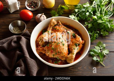 Ragoût de poulet aux tomates et aux herbes (chakhokhbili) dans un bol blanc sur une table en bois. Viande de poulet cuite au four avec sauce tomate. Alimentation saine et confortable. Fermer Banque D'Images