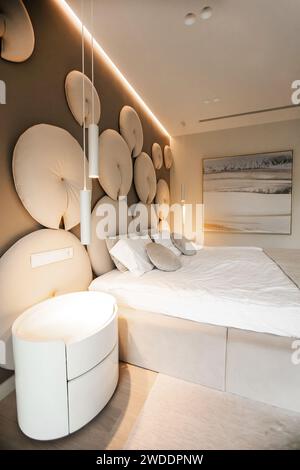 grand lit crémeux style maison moderne. Lit double avec oreillers, couverture moelleuse, moquette, lampe, fauteuil et meubles. intérieur de la chambre Banque D'Images