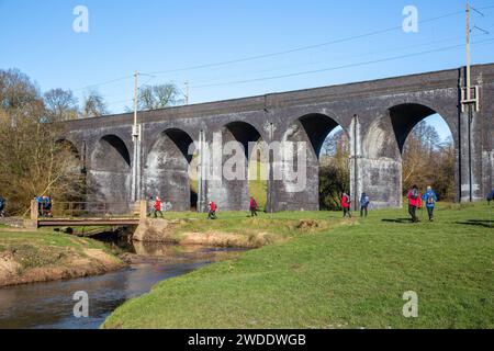 Groupe de randonneurs dans la campagne du Cheshire marchant le long de la rivière Dean approchant du viaduc de chemin de fer près de Wilmslow Cheshire Banque D'Images