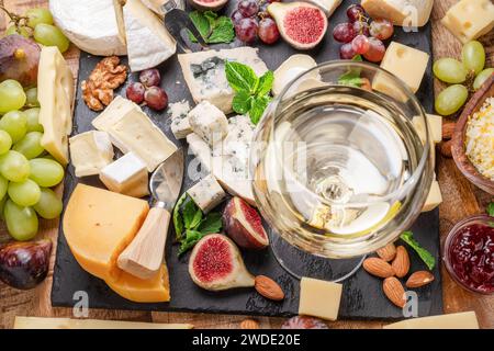 Verre de vin blanc avec une variété de fromages tranchés avec des fruits, menthe, noix et couteaux à couper le fromage. Merveilleux fond de vin et de fromage pour votre pr Banque D'Images