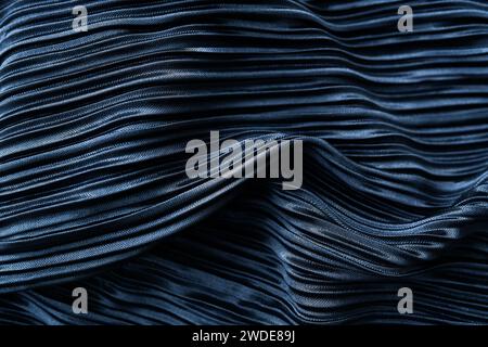 Un tissu plissé bleu foncé avec une texture brillante et des plis complexes. Il a une sensation artistique due au jeu de lumière et d'ombre sur les plis Banque D'Images