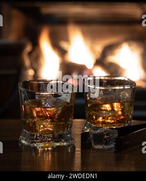Deux verres de whisky et de glace sur une table en bois avec cheminée brûlante en arrière-plan Banque D'Images