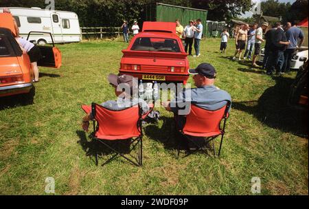 Les fiers propriétaires de leur Capri rouge vif se détendent au soleil au Meet. La Ford Capri a été présentée au salon de Bruxelles en janvier 1968 et est devenue une berline de sport populaire européenne basée sur la Mustang USA et initialement nommée «Pony». Ici, le club des supporters des membres de Capri BADGER’S HILL, EVESHAM se réunit un dimanche le 27 juillet 2008 avec des membres montrant leurs propriétaires prisés de cette superbe voiture à moteur conçue. Banque D'Images