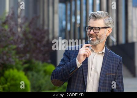 Homme professionnel senior en tenue d'affaires, l'air joyeux en dehors d'un cadre de bureau moderne, représentant la confiance et l'expérience. Banque D'Images