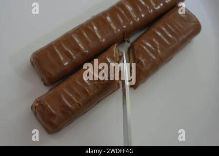 Bonbons, bâtonnets coupés au couteau recouverts de chocolat au lait, de foie sablé et de caramel placés sur une assiette en verre blanc. Banque D'Images