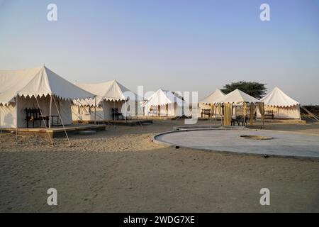Village de tentes touristiques dans le désert du Thar, devant un bus rouge, près de Jaisalmer, Rajasthan, Inde du Nord Banque D'Images