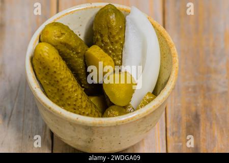 Gros plan d'un petit bol de cornichons et d'oignons assis sur le dessus de table en bois Banque D'Images