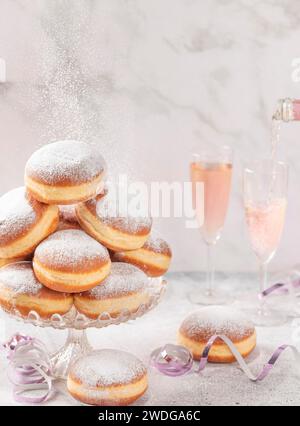 Beignets sur un support en verre, le vin mousseux rose est versé en arrière-plan, tombant du sucre glace Banque D'Images