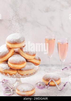 Beignets sur un support en verre avec vin mousseux rose en arrière-plan et sucre glace tombant Banque D'Images