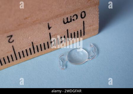 Photo d'une lentille itraoculaire pliable pour traiter la cataracte à côté d'une règle en bois Banque D'Images