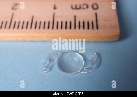 Photo d'une lentille itraoculaire pliable pour traiter la cataracte à côté d'une règle en bois Banque D'Images