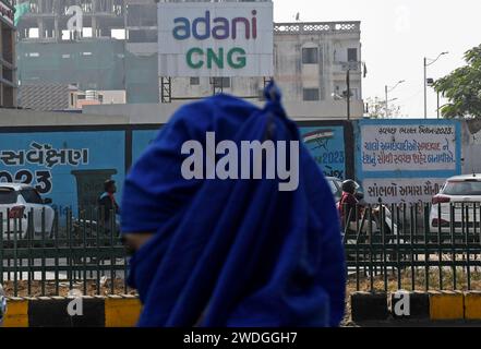 Une femme marche dans la rue devant le logo Adani CNG (gaz naturel comprimé) à Ahmedabad. Le GNC (gaz naturel comprimé) est utilisé dans de nombreux véhicules utilitaires et publics de nos jours pour des raisons environnementales et il est très rentable par rapport à l'essence qui devient très coûteuse. Banque D'Images