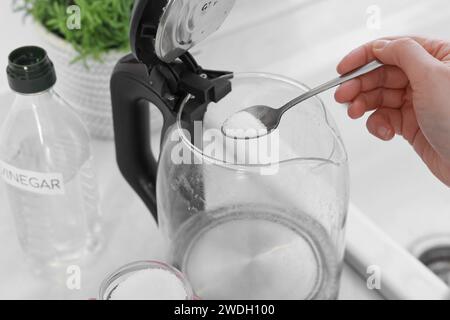 Femme ajoutant du bicarbonate de soude dans une bouilloire électrique dans la cuisine, closeup Banque D'Images