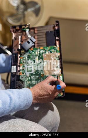 vieille femme avec un ordinateur portable sur ses genoux et un tournevis dans sa main essayant de le réparer Banque D'Images