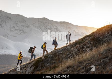 Groupe de jeunes randonneurs actifs avec des sacs à dos marche vers le haut dans les montagnes au coucher du soleil Banque D'Images