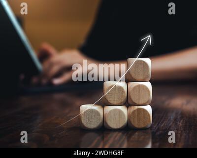 Flèche mince montante se développant sur des blocs de cube en bois comme étapes de graphique tout en tapant homme d'affaires avec un ordinateur portable tablette. Croissance du marché des entreprises, objectif A. Banque D'Images