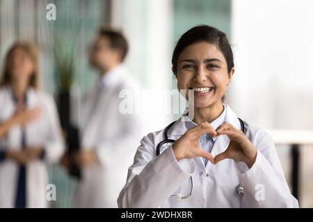 Joyeuse jeune femme médecin indienne faisant main coeur Banque D'Images