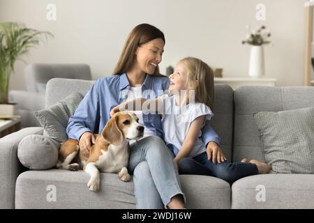 Heureuse belle mère embrassant l'enfant et touchant le chien sur le canapé Banque D'Images