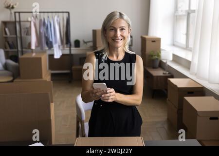 Femme d'âge moyen attrayante détient téléphone portable commandant des services de messagerie de livraison Banque D'Images