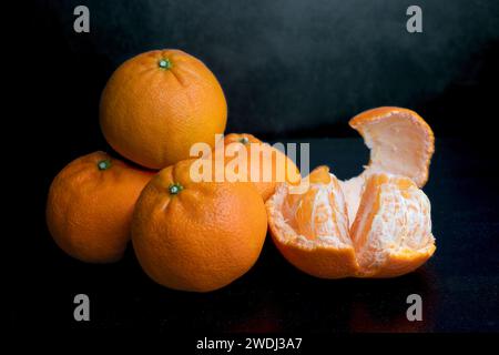 Une pile de quatre tangerines sur un fond sombre. Fruits orange sur fond noir. Agrumes dans la cuisine. Une pile de quatre mandarines sur un dos sombre Banque D'Images