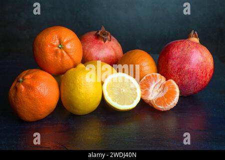 Mandarines, citron et grenade sur fond noir foncé, graphite. Fruits sains. La santé dans la cuisine. Fruits tropicaux. Banque D'Images