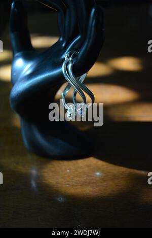 Statuette noire d'une main féminine mate avec boucles d'oreilles en argent avec de belles pierres et un pendentif. Banque D'Images