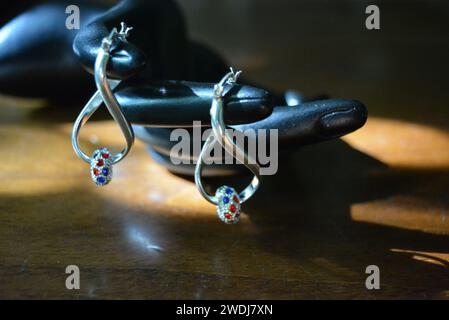 Statuette noire d'une main féminine mate avec boucles d'oreilles en argent avec de belles pierres et un pendentif. Banque D'Images