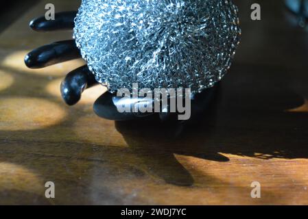 Statuette noire d'une main féminine mate avec une éponge métallique sur une table en bois brun de style ancien avec les rayons du soleil. Banque D'Images
