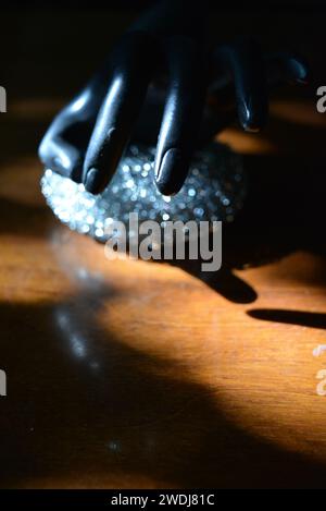 Statuette noire d'une main féminine mate avec une éponge métallique sur une table en bois brun de style ancien avec les rayons du soleil. Banque D'Images