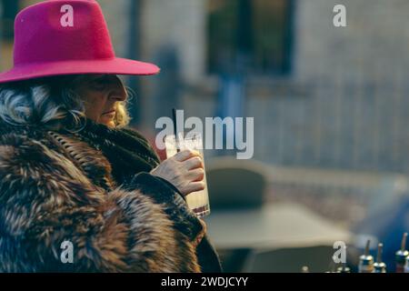 femme senior de classe européenne de l'est boire sirotez un cocktail tom collins en plein air en hiver lors d'un événement privé Banque D'Images