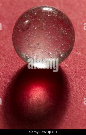 Un marbre de verre clair avec des bulles sur un fond rouge. Banque D'Images