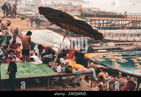 Un moine Saint, un sadhu assis sur le remblai de Varanasi ghat, sous un parapluie au petit matin. Photographies prises à distance. Uttar Prad Banque D'Images