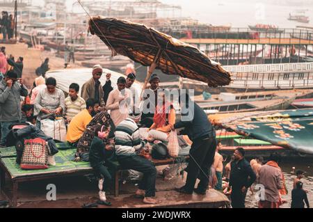 Un moine Saint, un sadhu assis sur le remblai de Varanasi ghat, sous un parapluie au petit matin. Photographies prises à distance. Uttar Prad Banque D'Images