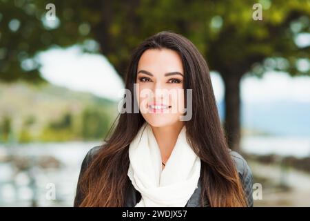 Portrait en plein air de belle femme brune aux cheveux longs, portant une grande écharpe en cachemire blanc et une veste en cuir noir Banque D'Images