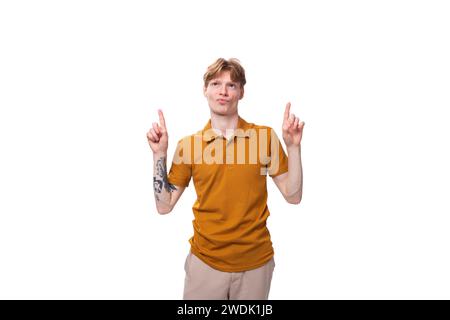 jeune étudiant à la mode avec les cheveux rouges courts habillé d'un t-shirt jaune est activement gestuant Banque D'Images