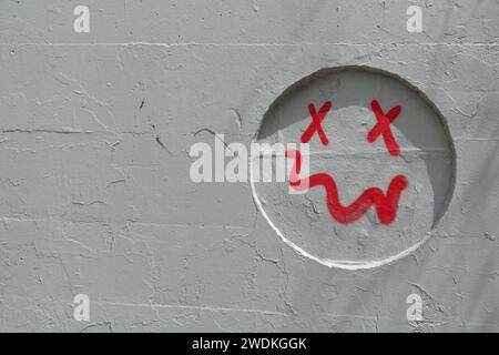 Visage souriant simple avec un spray buccal tordu peint sur un renfoncement mural gris. Arrière-plan abstrait. Banque D'Images
