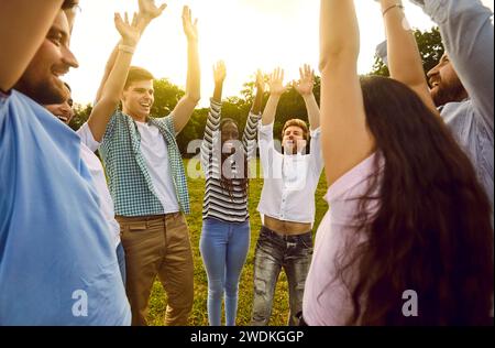 Heureux étudiants amis debout ensemble à l'extérieur dans le parc d'été levant les mains vers le haut appréciant la réunion. Banque D'Images