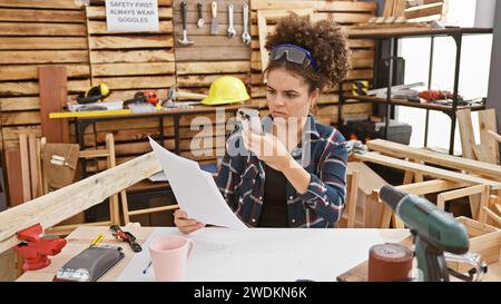 Une jeune femme examine des documents dans un atelier de menuiserie, entourée d'outils et de bois. Banque D'Images