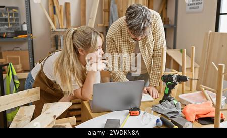 Un homme et une femme collaborent dans un atelier de menuiserie entouré d’outils et de meubles inachevés. Banque D'Images