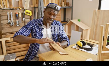 Homme afro-américain examine le bois dans l'atelier avec des outils Banque D'Images