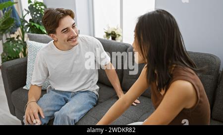 Un homme et une femme s'assoient étroitement sur un canapé dans leur appartement moderne, partageant un moment joyeux. Banque D'Images