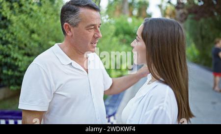 Un père et une fille hispaniques confiants s'engagent dans une conversation chaleureuse, debout ensemble, souriant, rayonnant la positivité au cœur du parc ensoleillé Banque D'Images