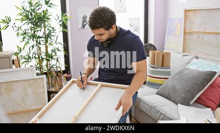 Un jeune homme avec une barbe assemble un cadre en toile dans un environnement de studio intérieur lumineux et inspiré de l'art. Banque D'Images