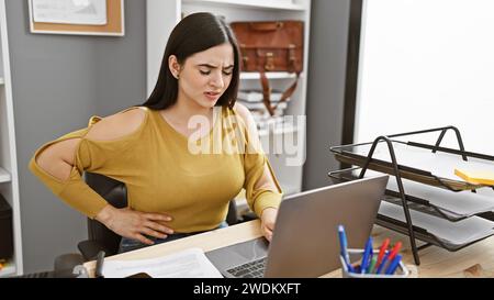 Une jeune femme grimaque avec des douleurs à l'estomac dans un bureau moderne. Banque D'Images